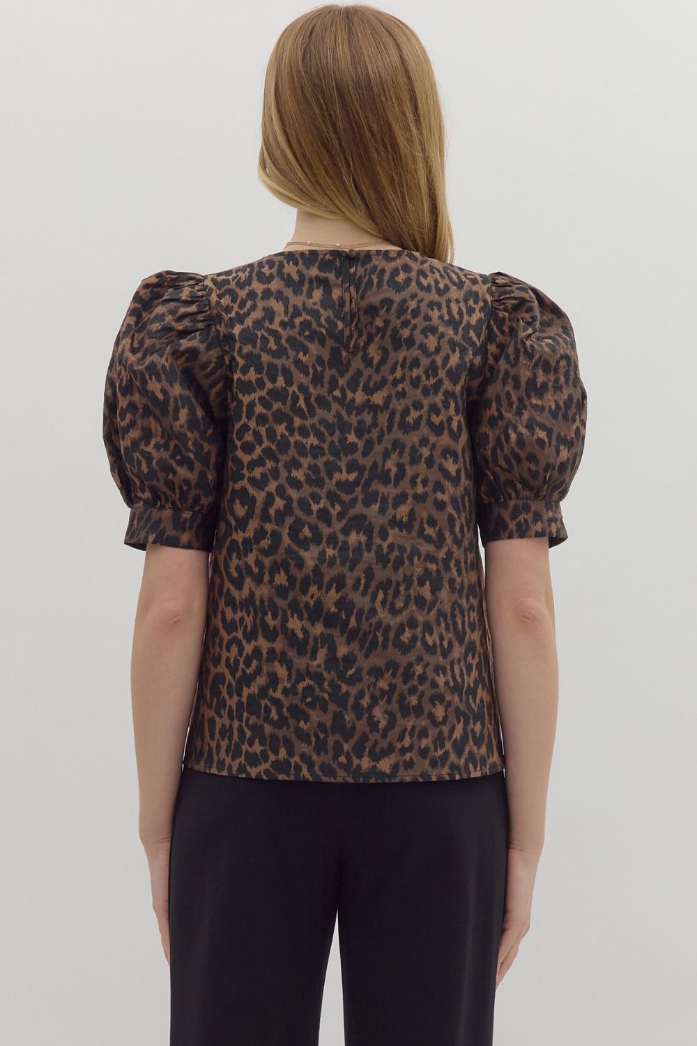 Person wearing a leopard print top with puffed sleeves on a plain background