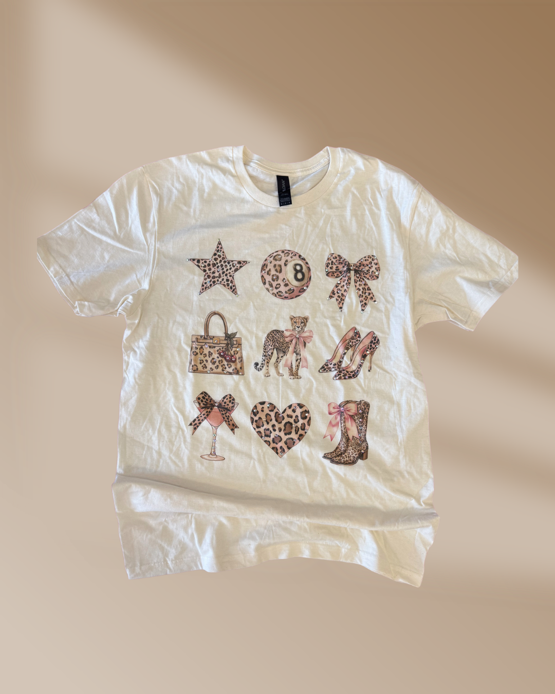 White t-shirt with various cheetah print graphic designs on a beige background
