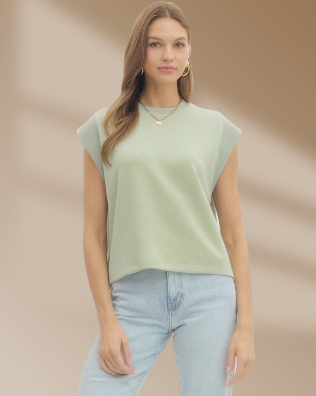 Woman wearing a light green sleeveless top and light blue jeans against a beige background