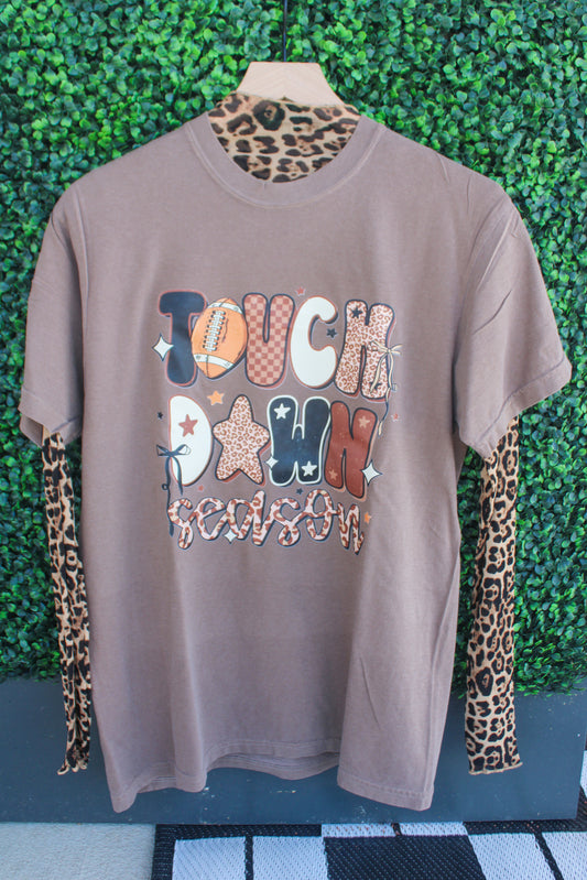 Brown t-shirt with colorful text and patterns on a mannequin against a green leafy background